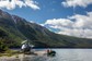A helicopter parked in a remote river valley with two fishers on a small boat.
